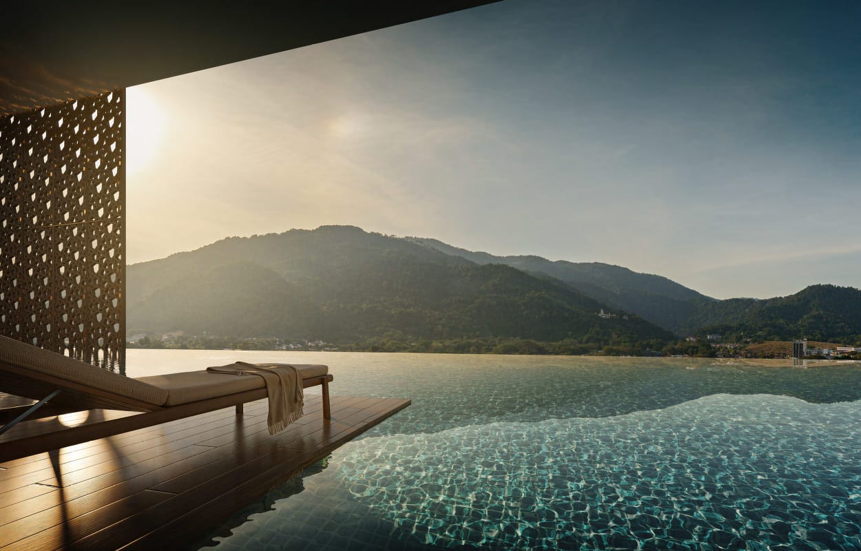 Infinity pool with timber deck and lounger overlooking Penang's green hills