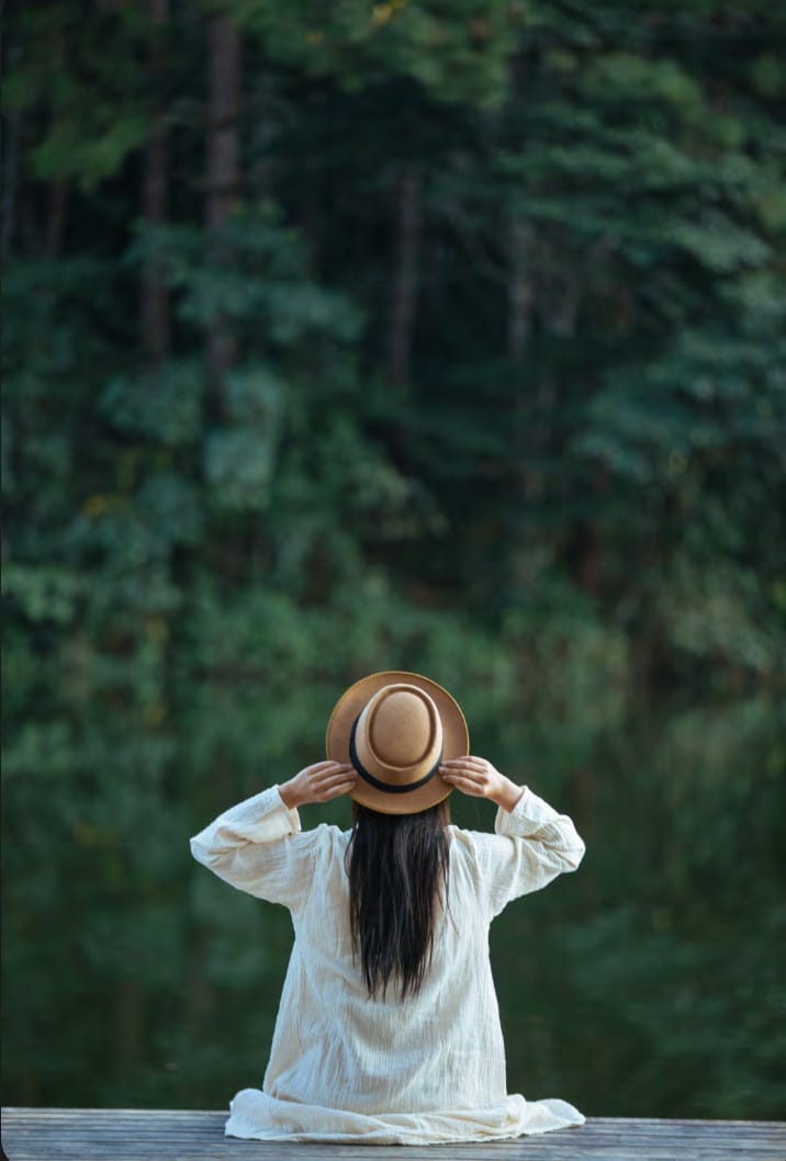 Woman in a sun hat relaxing by a forest lake